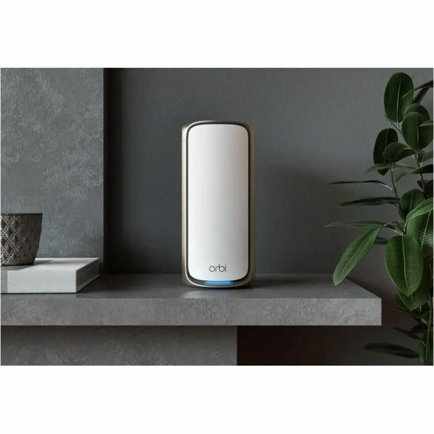 Netgear Orbi ORBI9QB WiFi7 router on a shelf, white body with brown edges and blue base light