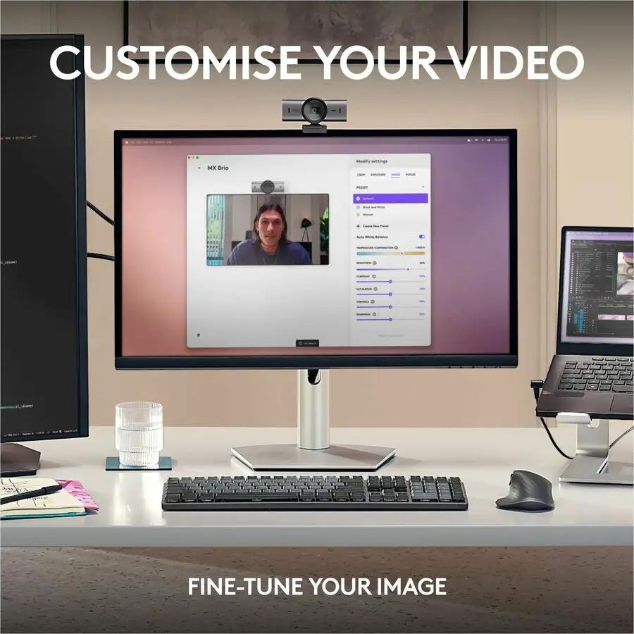 Logitech MX BRIO webcam on top of a computer monitor in a desk setup with keyboard and laptop, black