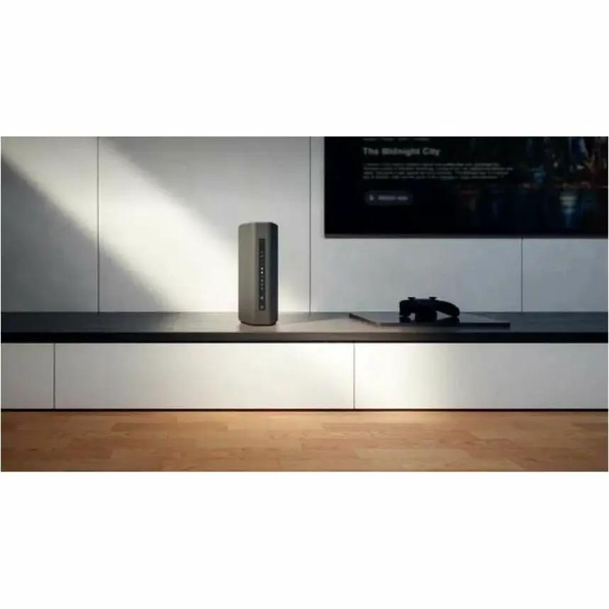 Netgear Nighthawk RS300 router on a living-room shelf, silver vertical unit with LED indicators.