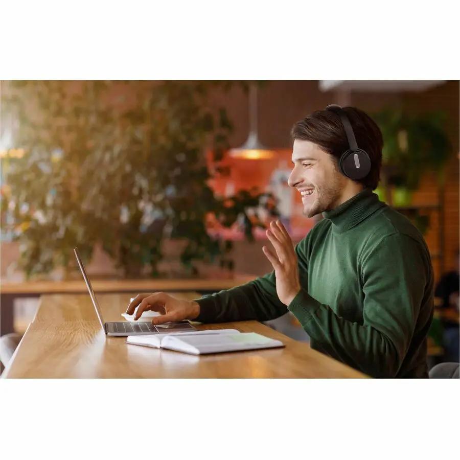 Yealink BH70 Dual UC USB-C/A headset, black, worn by a man at a wooden desk with a laptop.