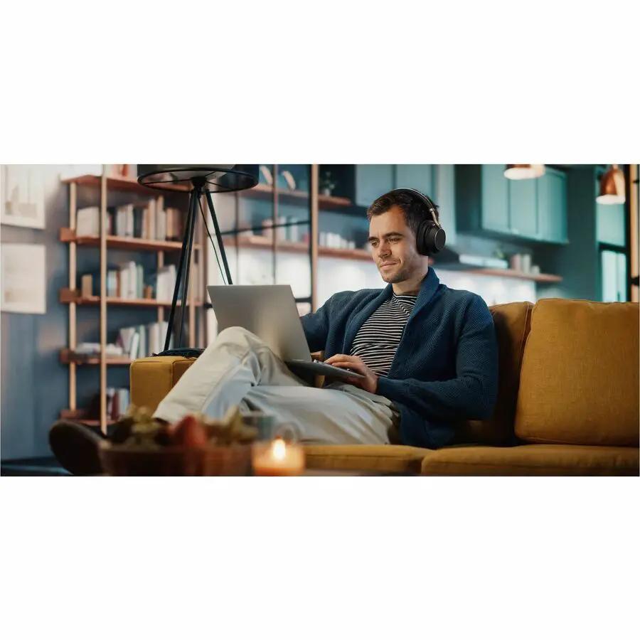 Yealink BH76 USB headset, black, worn by man on sofa using a laptop