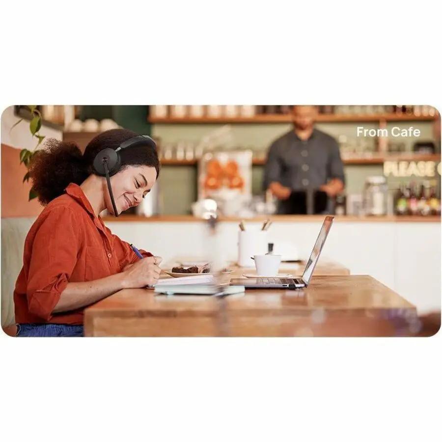 Yealink BH74 UC USB-C A headset; black, worn by a person at a cafe using a laptop.