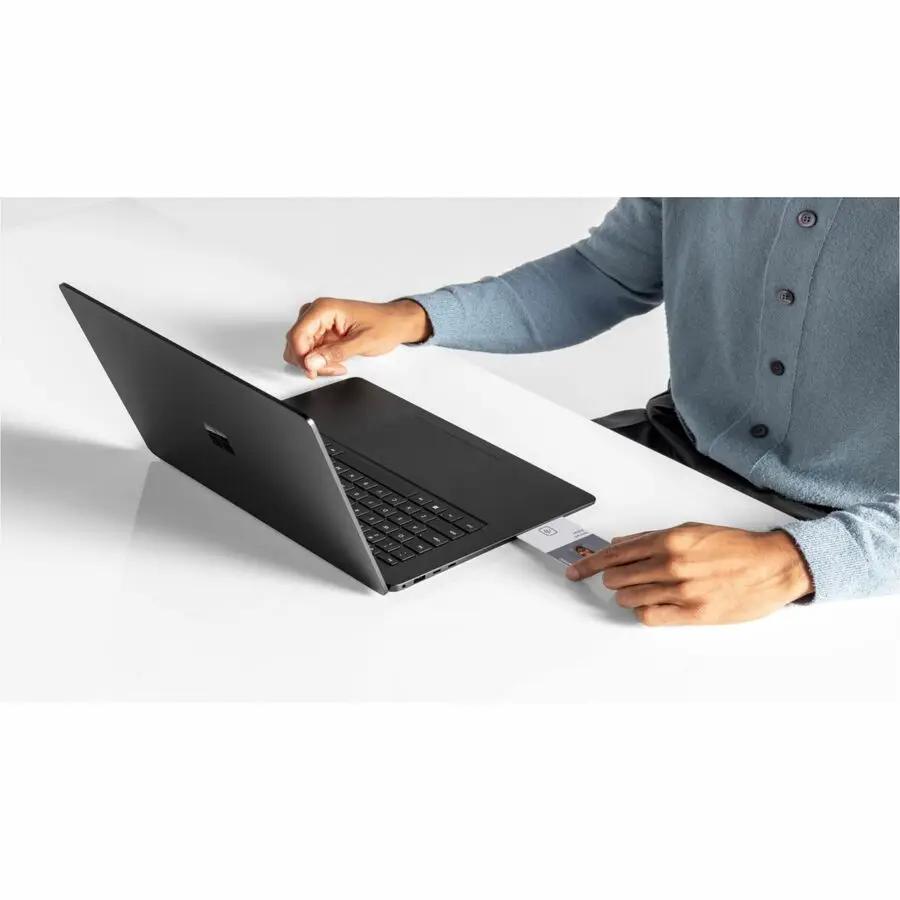 Microsoft Surface Laptop 7 15-inch touchscreen laptop in black on a white desk, with a card held near the keyboard.
