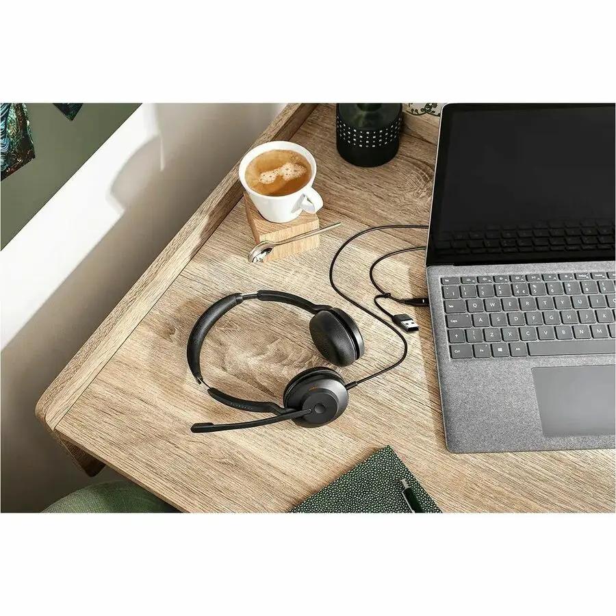 Jabra Evolve2 30 SE headset on a wooden desk beside a laptop; black over-ear with boom mic