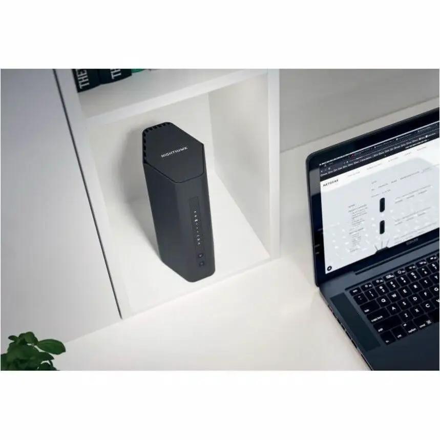 NETGEAR Nighthawk RS150 Gigabit WiFi 7 router on a white shelf beside a laptop
