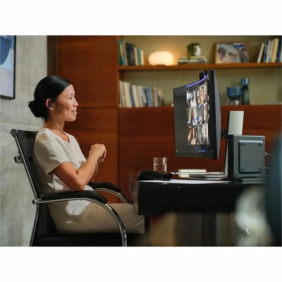 HP EliteDesk 8 G1a black mini desktop at a desk with curved screen displaying conference; woman wearing headset seated
