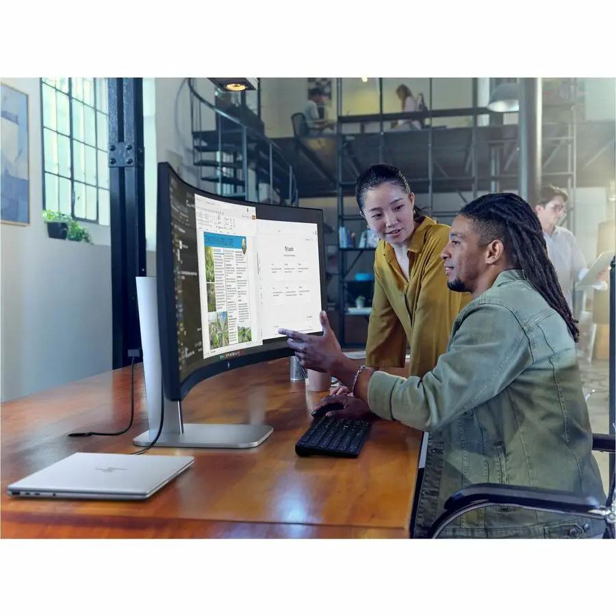 HP EliteDisplay 549pm 49-inch curved LED monitor on a wooden desk with two coworkers viewing the screen.