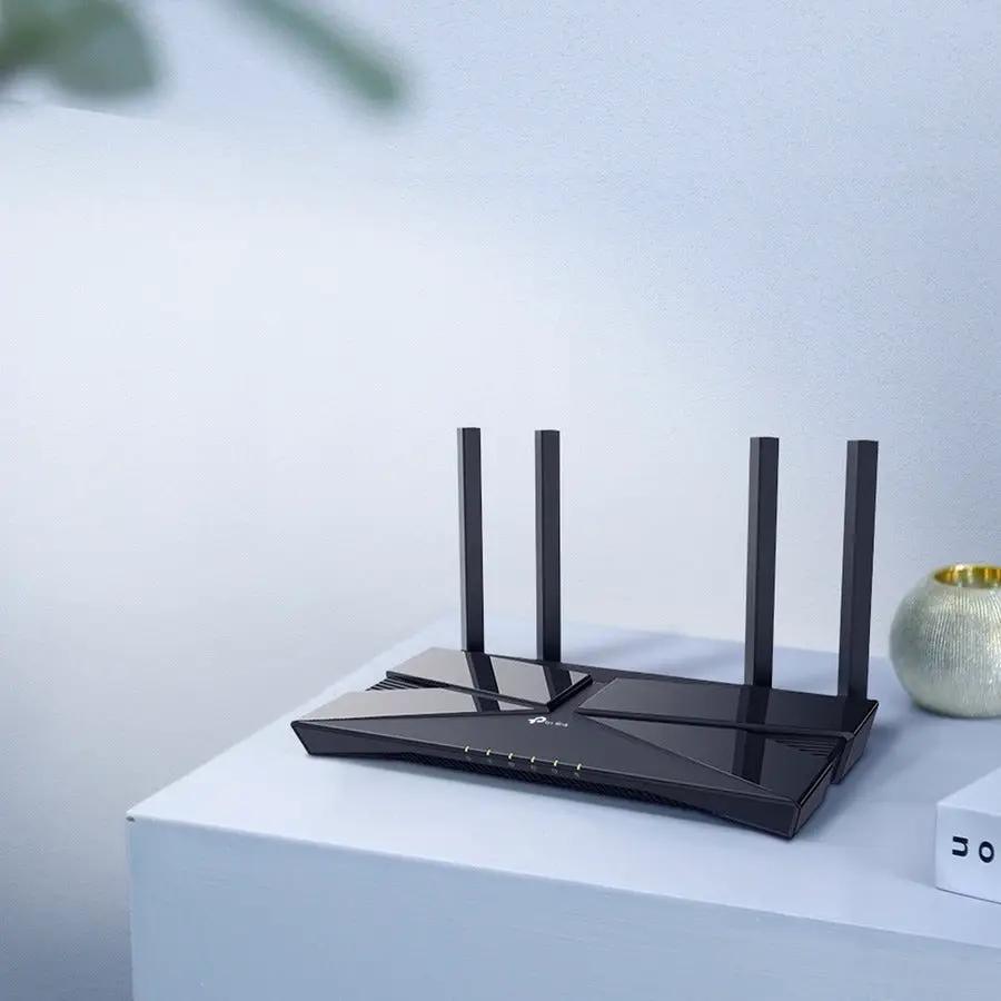 TP-Link Archer AX10 WiFi 6 router with four antennas, black, on a white desk.