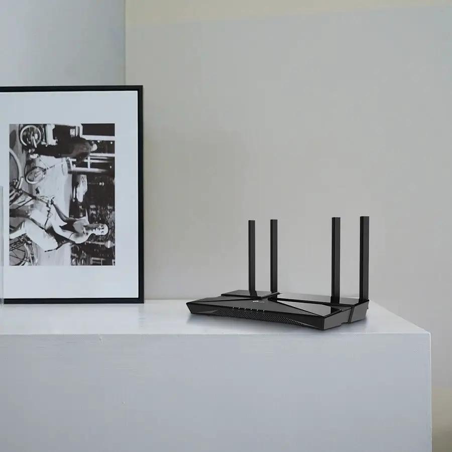 TP-Link Archer AX10 WiFi 6 router, black with four antennas on a white shelf beside a framed photo.