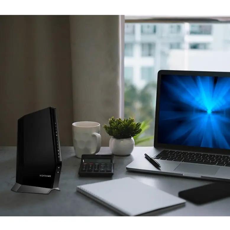 Netgear Nighthawk CAX80 router (black) on desk beside a laptop.