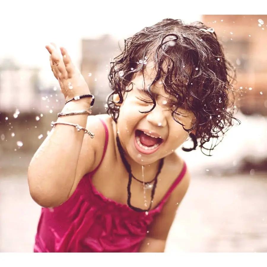 Child in pink sleeveless top laughing as water splashes outdoors