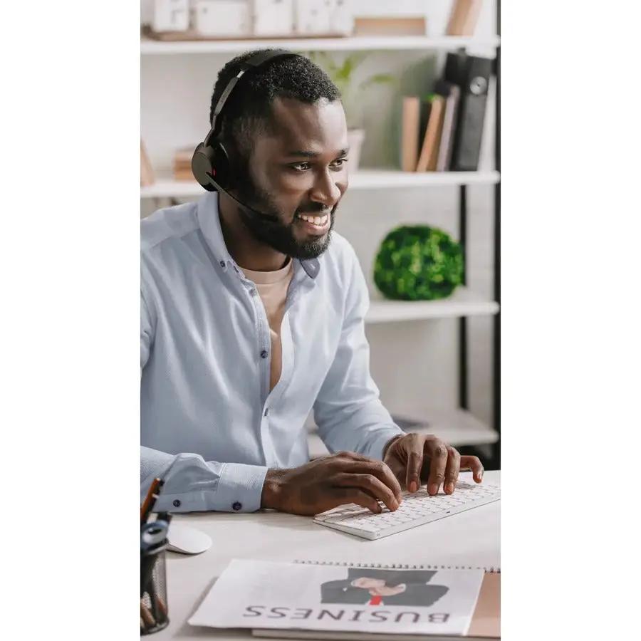 Jabra Evolve2 55 headset worn by man at a desk, typing on a white keyboard.