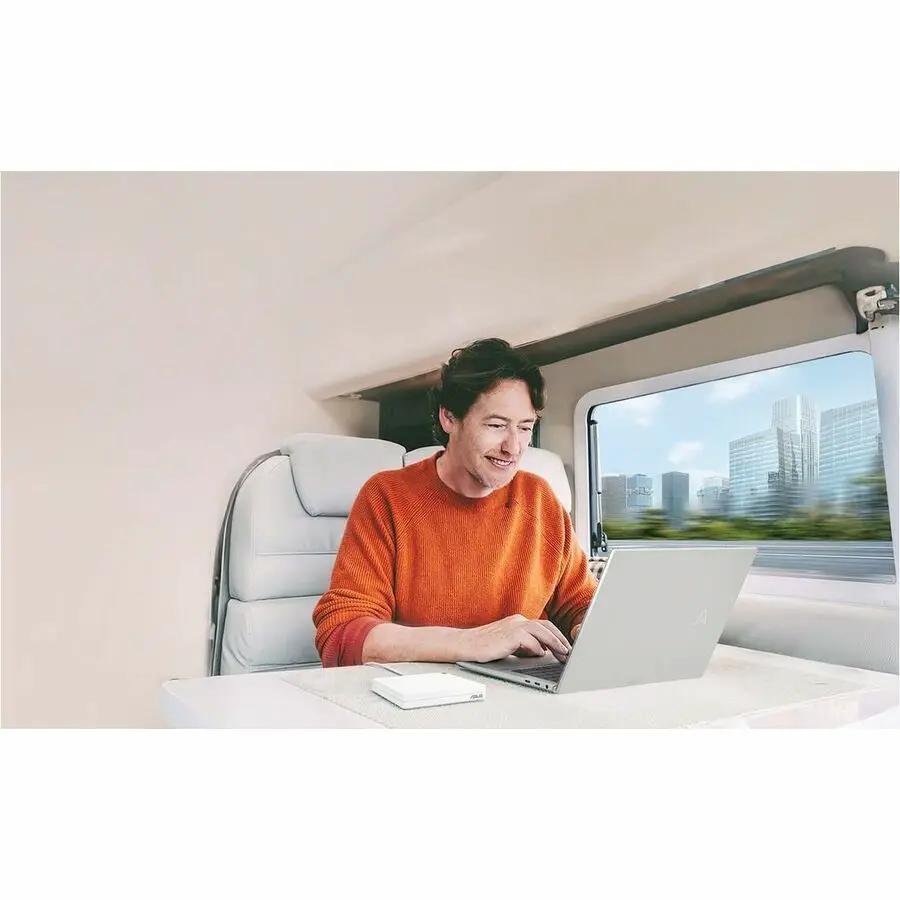 ASUS AX3000 DualBand WiFi6 VPN Router on a white table inside a vehicle with a man using a laptop.