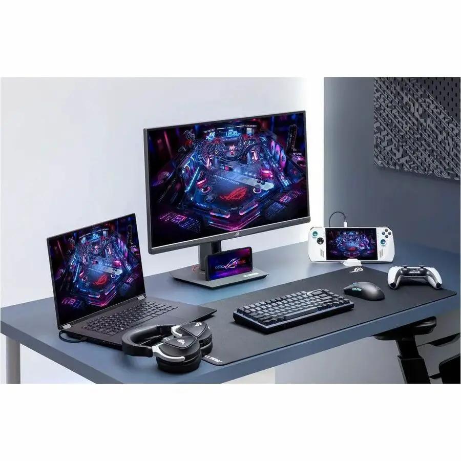 ASUS ROG Strix XG27ACMG 27-inch WQHD gaming monitor on desk with laptop, keyboard, headset and handheld console