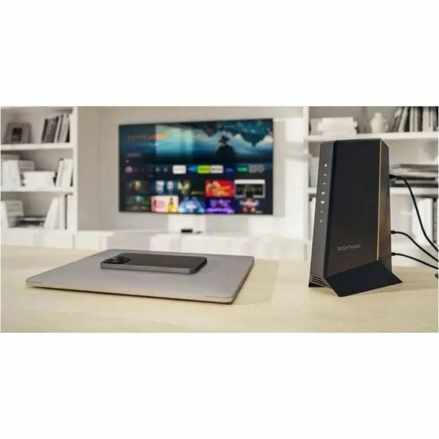 Netgear Nighthawk CM3000 2.5G unmanaged gateway modem, black, on desk with laptop