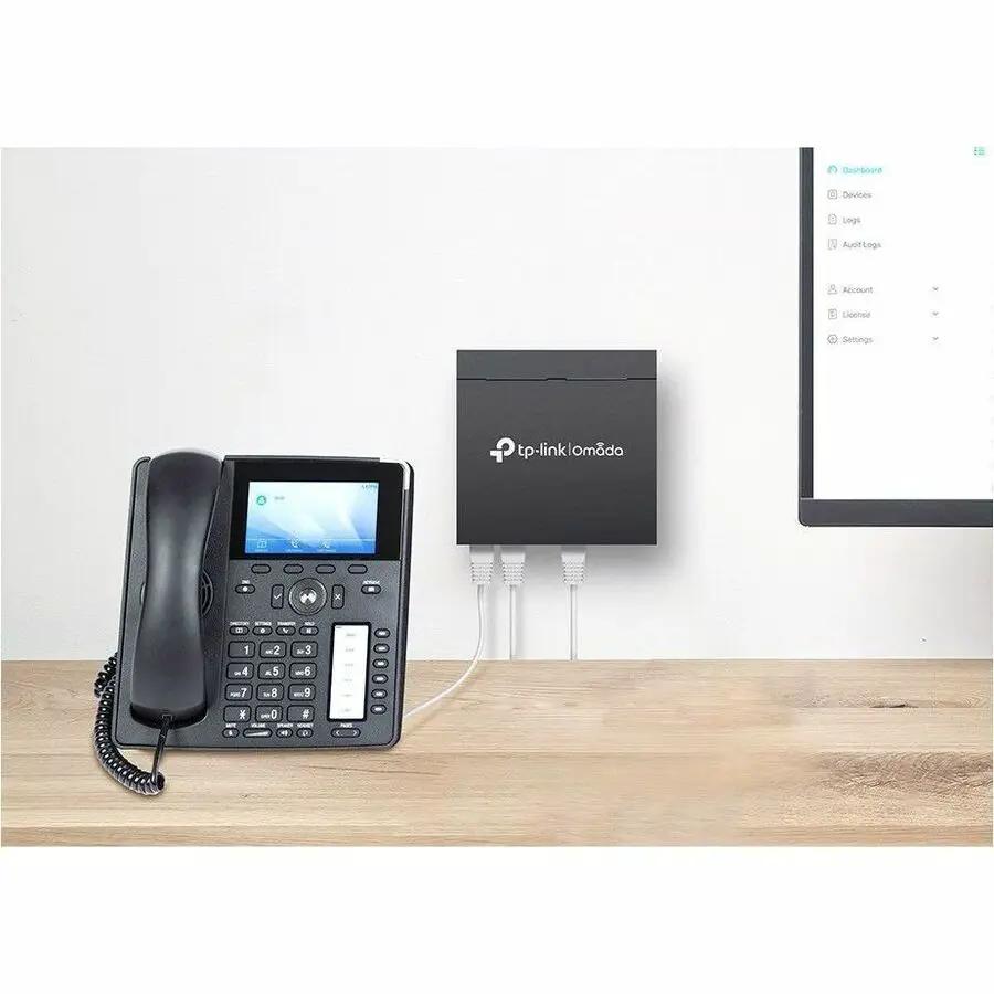 TP-Link Omada 5-Port Gigabit PoE+ Managed Switch on a wooden desk beside a desk phone and monitor.