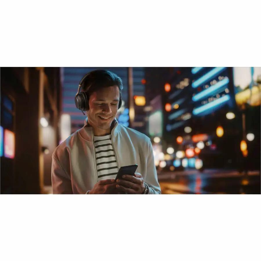 Yealink BH76PLSTMSUSBC/A over-ear headset, black, worn by man using a smartphone in a nighttime city street.