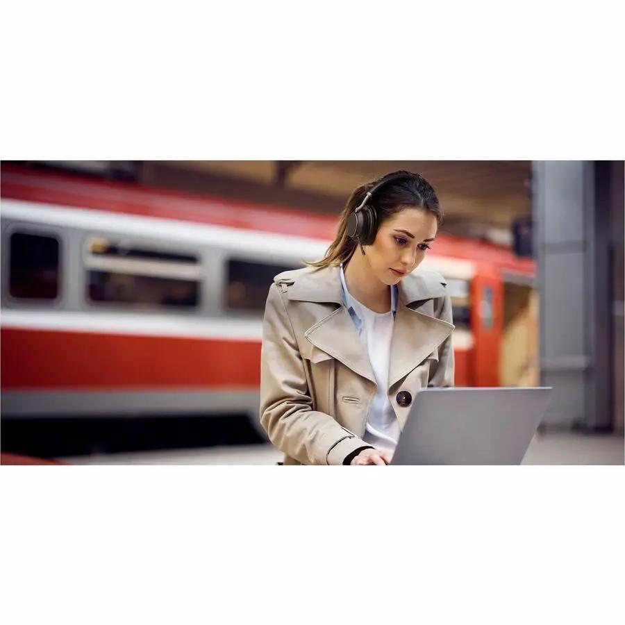 Yealink BH76PLSTMSUSBC/A black headset worn by woman at a train platform using a laptop