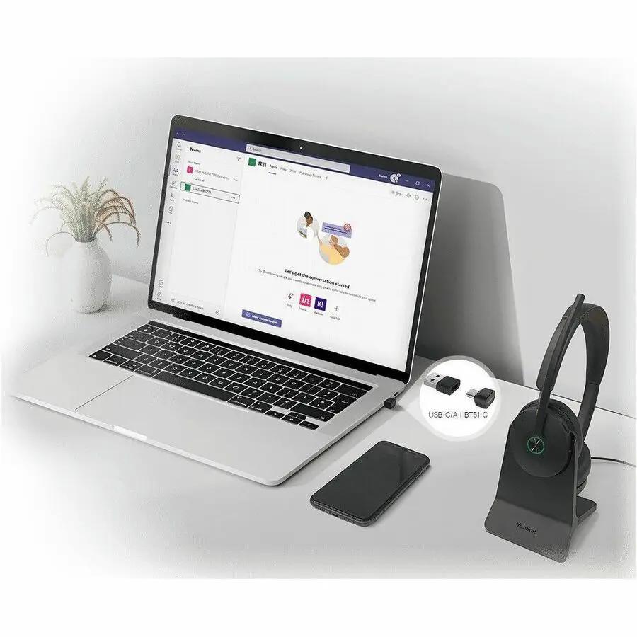 Yealink BH74 UC USB-C A wireless headset on a desk stand beside a laptop and smartphone