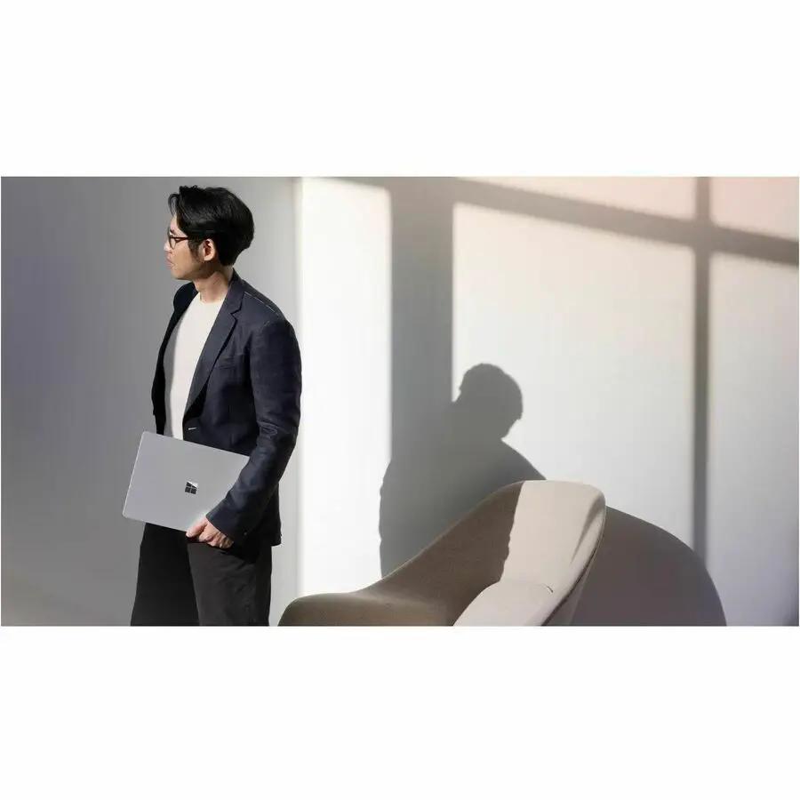 Microsoft Surface Laptop 7 silver laptop held by a man in a blazer in a bright office.
