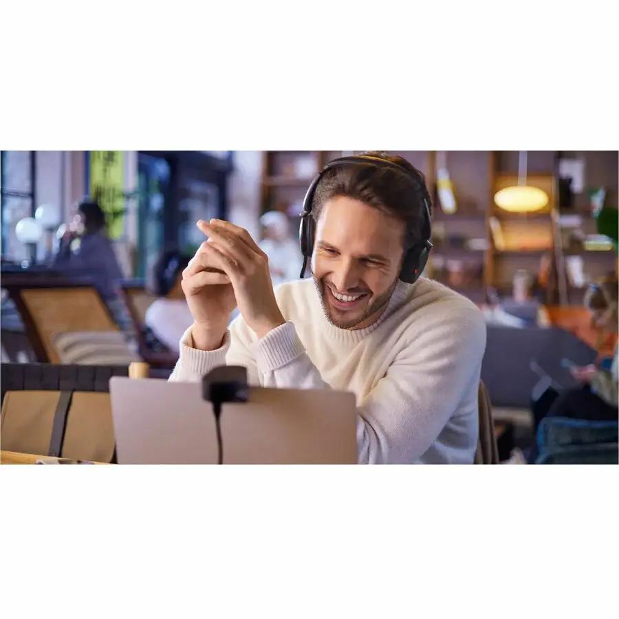Jabra Evolve2 30 SE headset, black over-ear, worn by man at a cafe with a laptop.