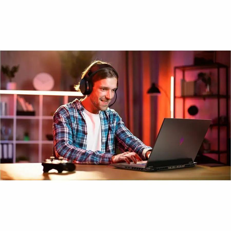 Acer Nitro V gaming laptop on a desk, black 16-inch display, person wearing a headset