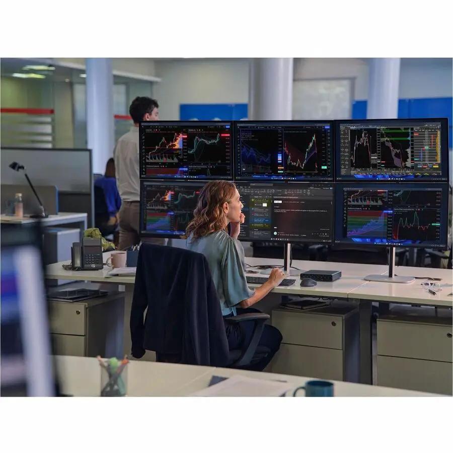 Desktop workspace with six widescreen monitors showing stock charts; a person is seated at a desk in an open office.