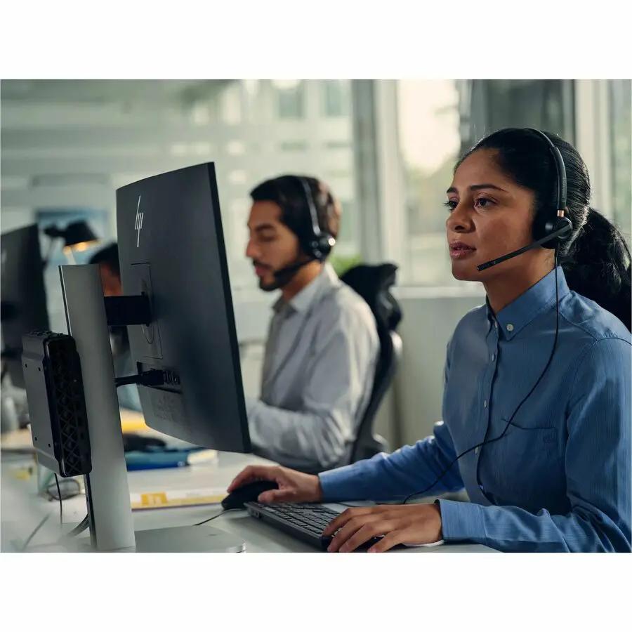 HP ProDesk 4 Mini G1i PC, compact desktop, in an office with two staff at desks wearing headsets.